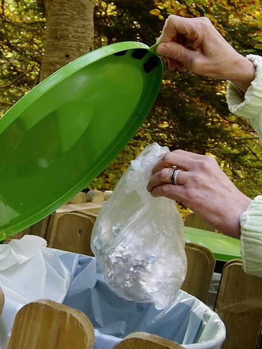 Plastikmüll wird in eine grüne Tonne geworfen.