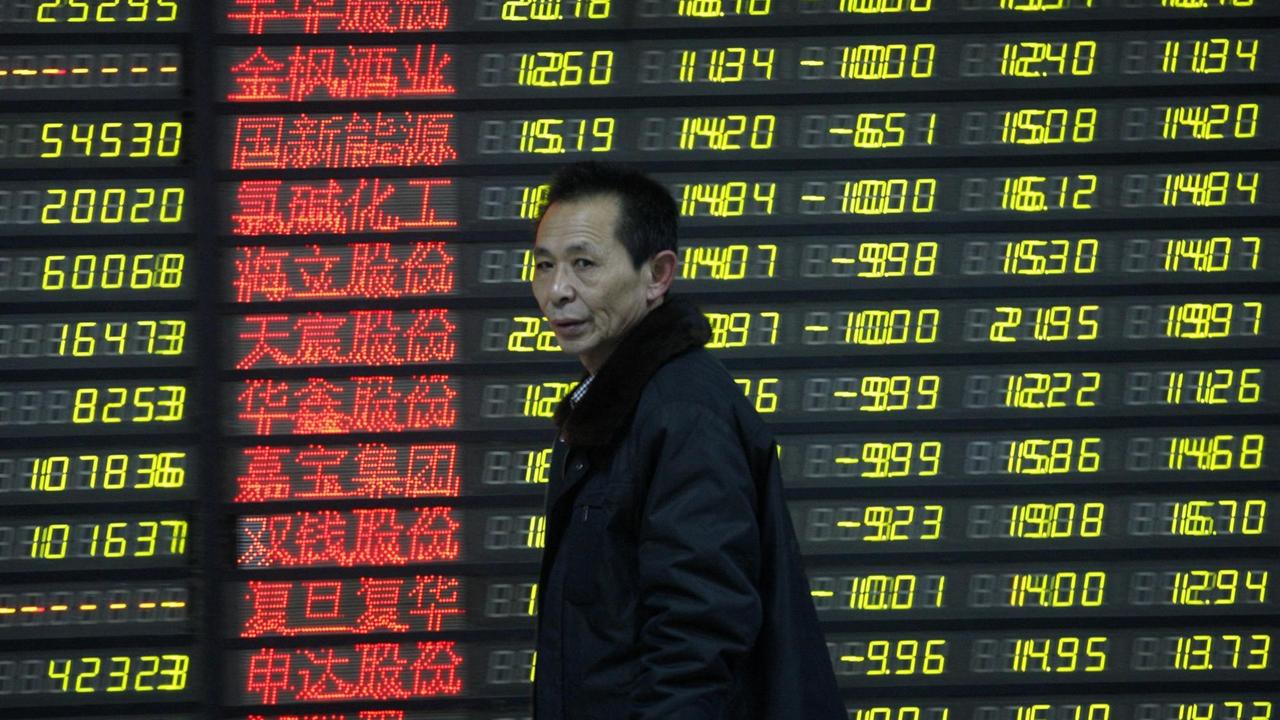 Ein Mann geht an einer Tafel mit Börsendaten in roten chinesischen Buchstaben und gelben Zahlen vorbei.