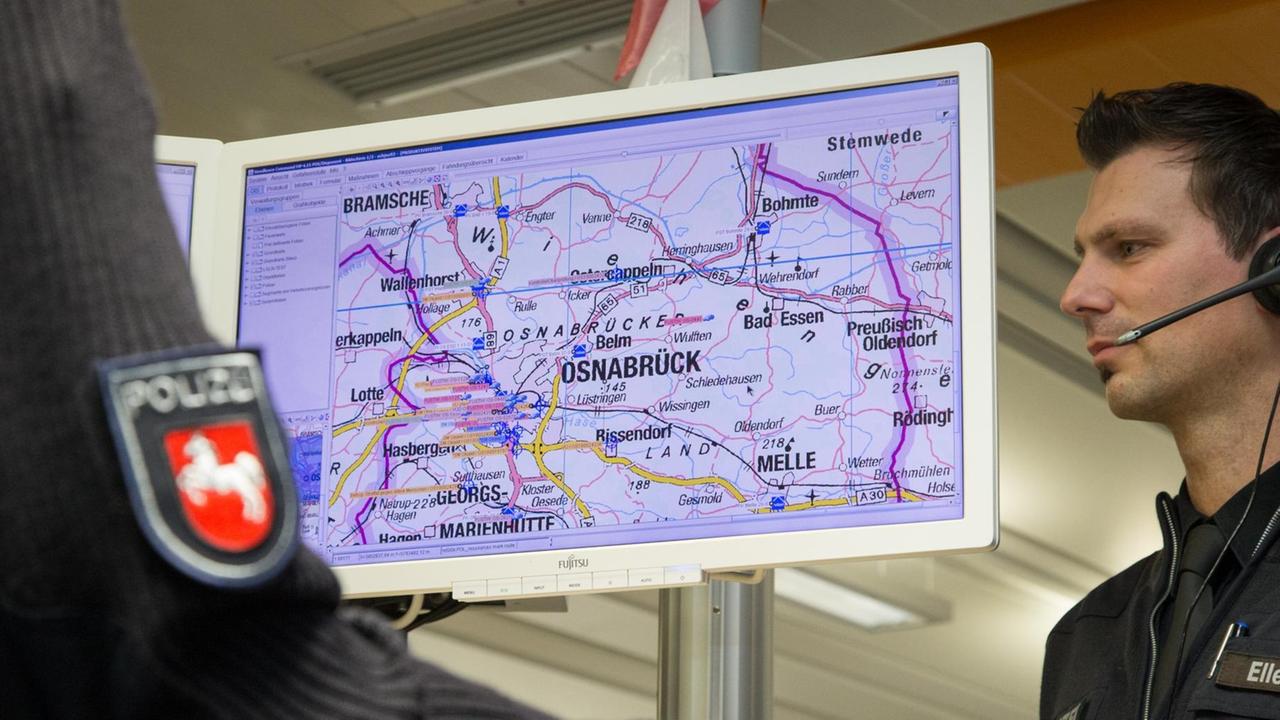 Ein Polizeibeamter steht mit einem headset an einem Notrufarbeitsplatz in der Leitstelle vom Landkreis Osnabrück und blickt auf eine Karte. 