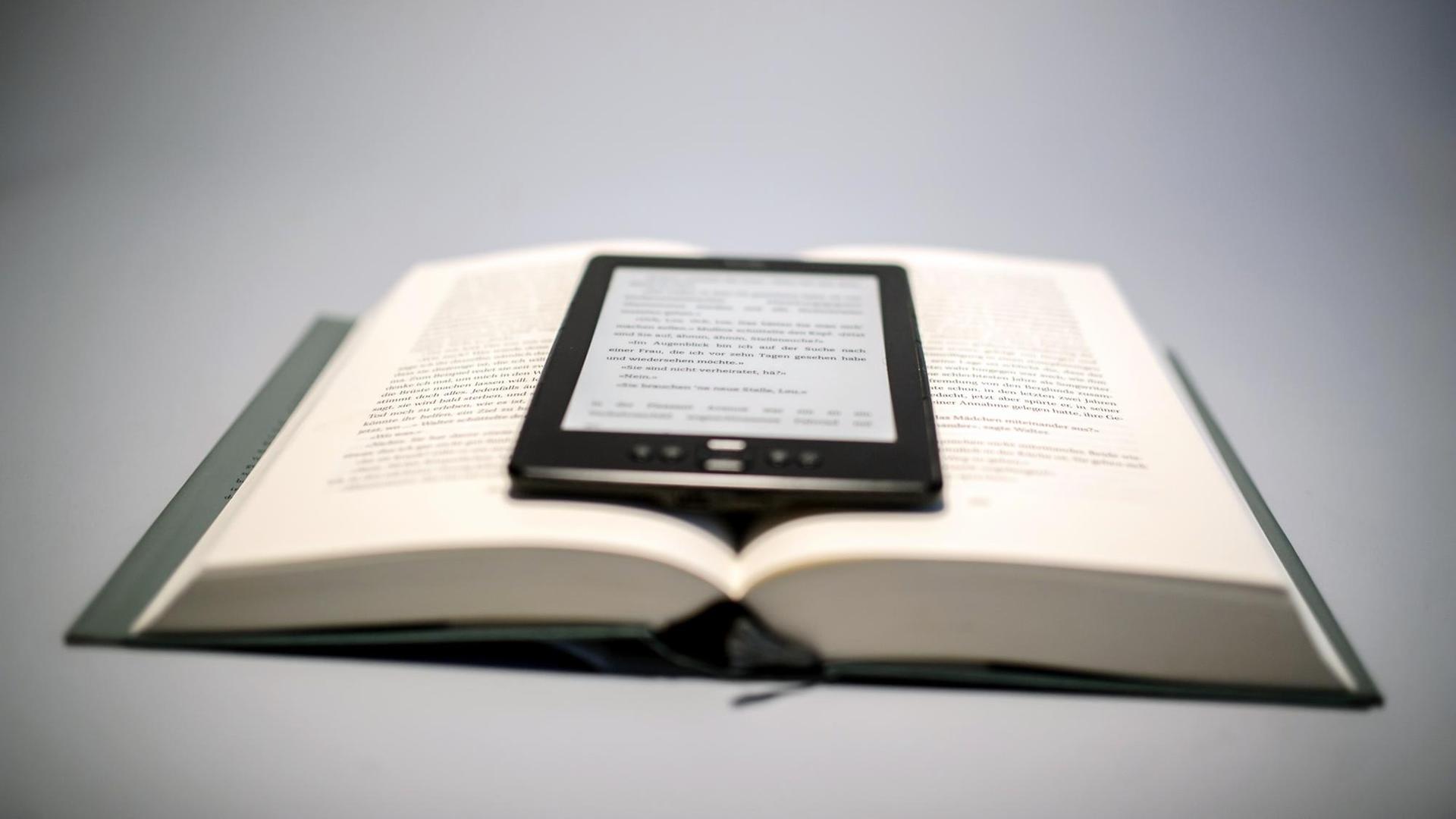 Ein E-Book-Reader liegt auf einem aufgeschlagenen Buch