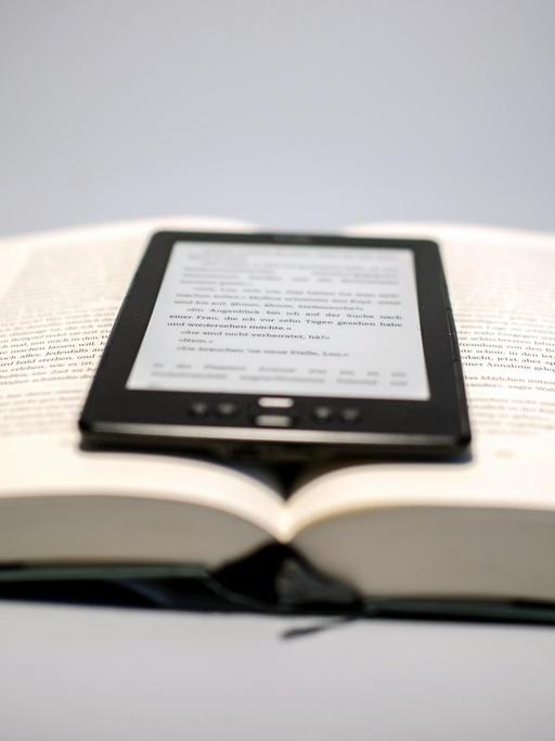 Ein E-Book-Reader liegt auf einem aufgeschlagenen Buch