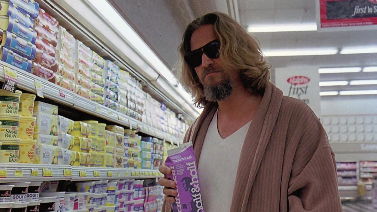Schauspieler Jeff Bridges steht mit Bademantel und Sonnenbrille im Film "The Big Lebowski" an einem Supermarktregal und trinkt Milch aus der Packung.