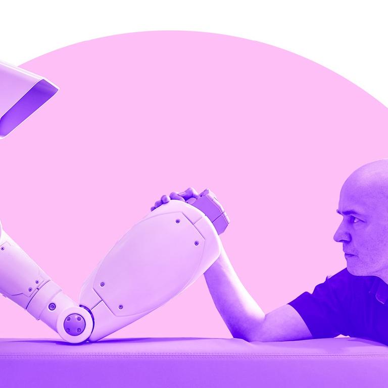 Ein Roboter und ein Mann mit kurzen Haaren sitzen sich an einem Tisch gegenüber und tragen einen Wettkampf im Armdrücken aus.
