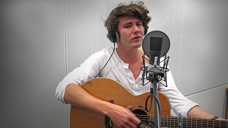 Faber mit Gitarre und Kopfhörern vor einem Mikrofon im Studio