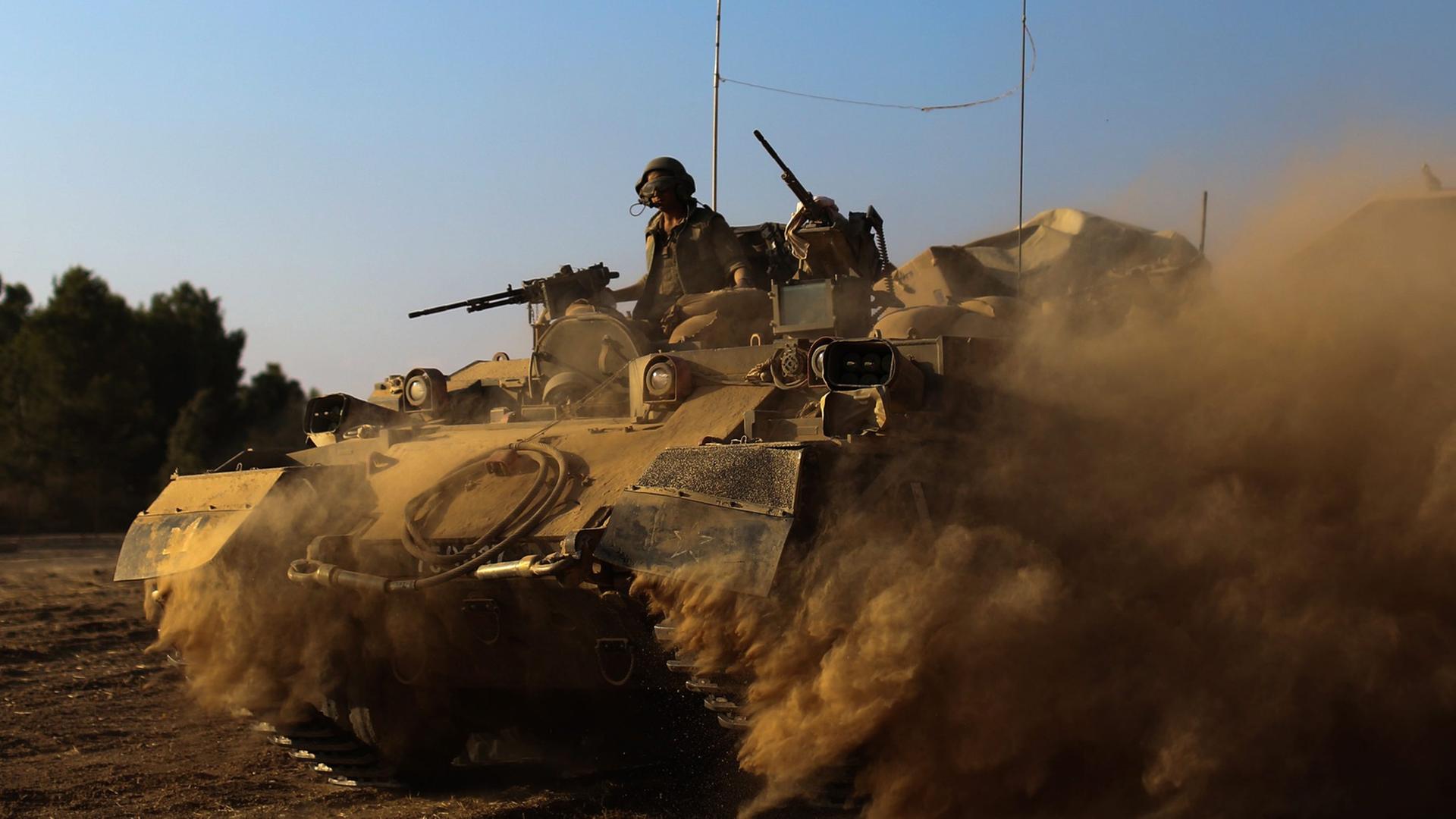 Israelische Soldaten mit Maschinengewehren fahren in einem Panzer, der reichlich Staub aufwirbelt, auf ihm steckt eine israelische Flagge Israelische Soldaten mit Maschinengewehren fahren in einem Panzer, der reichlich Staub aufwirbelt, auf ihm steckt eine israelische Flagge