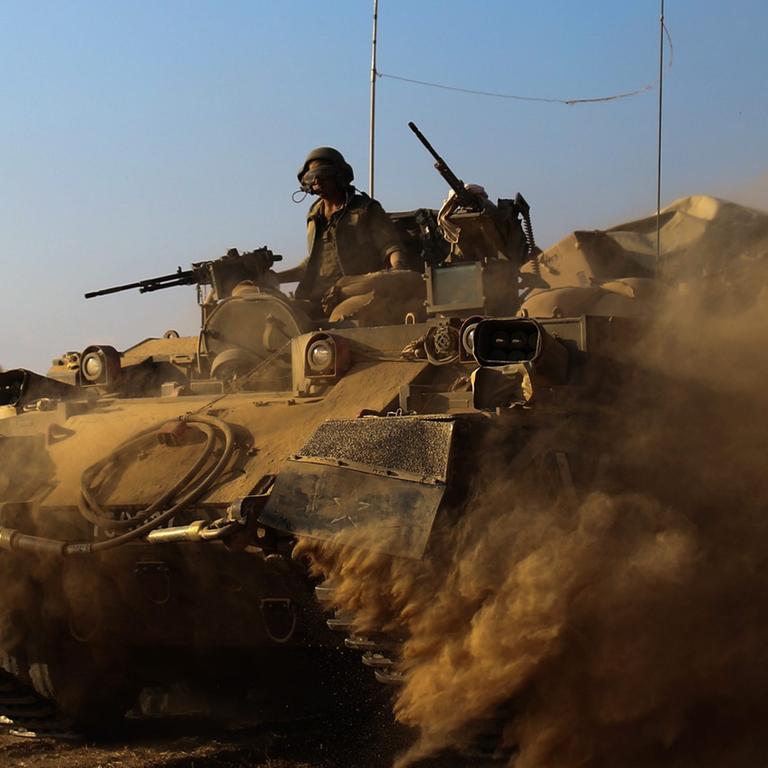 Israelische Soldaten mit Maschinengewehren fahren in einem Panzer, der reichlich Staub aufwirbelt, auf ihm steckt eine israelische Flagge