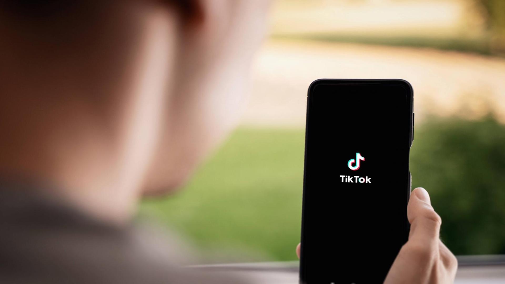 Ein junger Mensch hält ein Smartphone in der Hand, auf dem TikTok-App zu sehen ist.