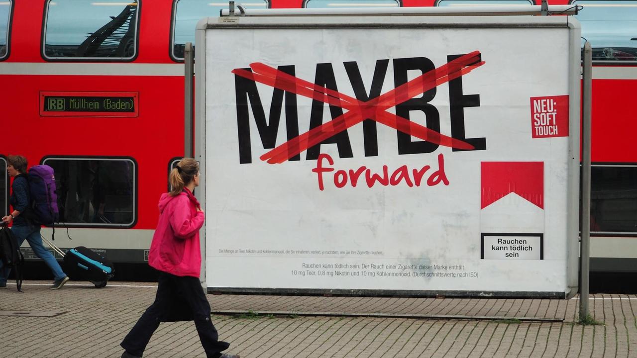 Auf dem weißen Plakat steht "Maybe forward", das erste Wort ist mit einem roten Kreuz durchgestrichen. Im Hintergrund steht ein Zug.
