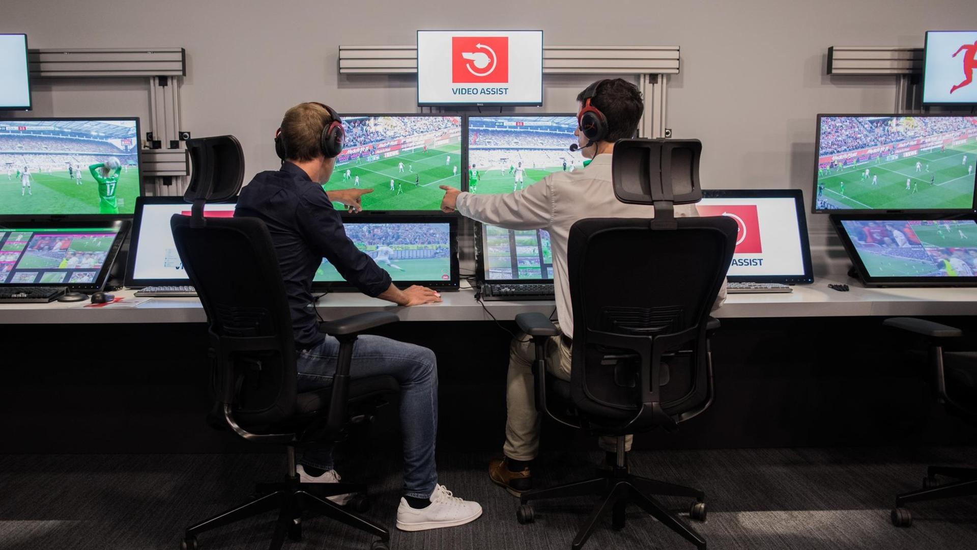 Der Schiedsrichter Sascha Stegemann (l) und ein Operator sitzen in einem Videoassistcenter vor Monitoren, die Spielszenen zeigen.