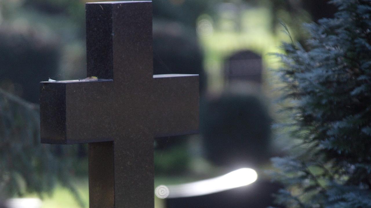 Ein Kreuz als Grabstein auf einem Friedhof.