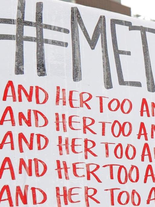 Eine Demonstrantin hält ein Schild mit dem Twitter-Hashtag #MeToo und der sich wiederholenden Aufschrift "and her too" in die Höhe.