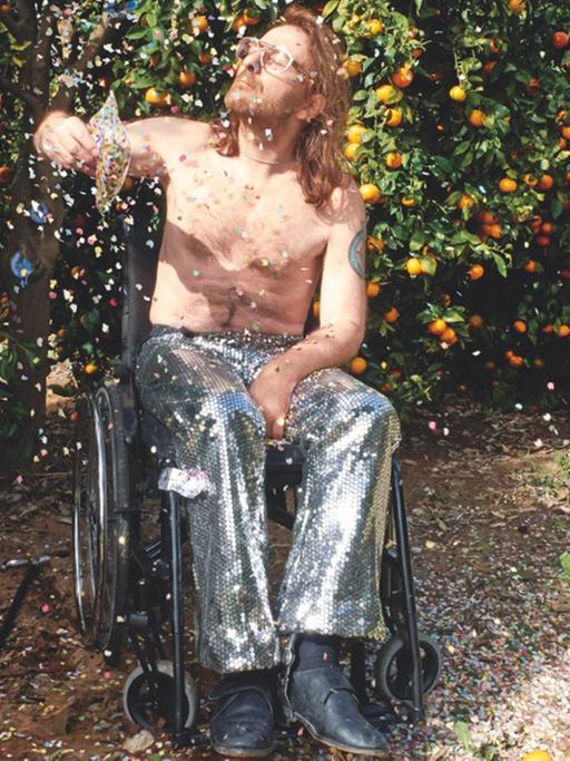Der Fotograf Daniel Josefsohn im Rollstuhl - freier Oberkörper, silberne Hose, die Augen geschlossen - bewirft sich mit Konfetti