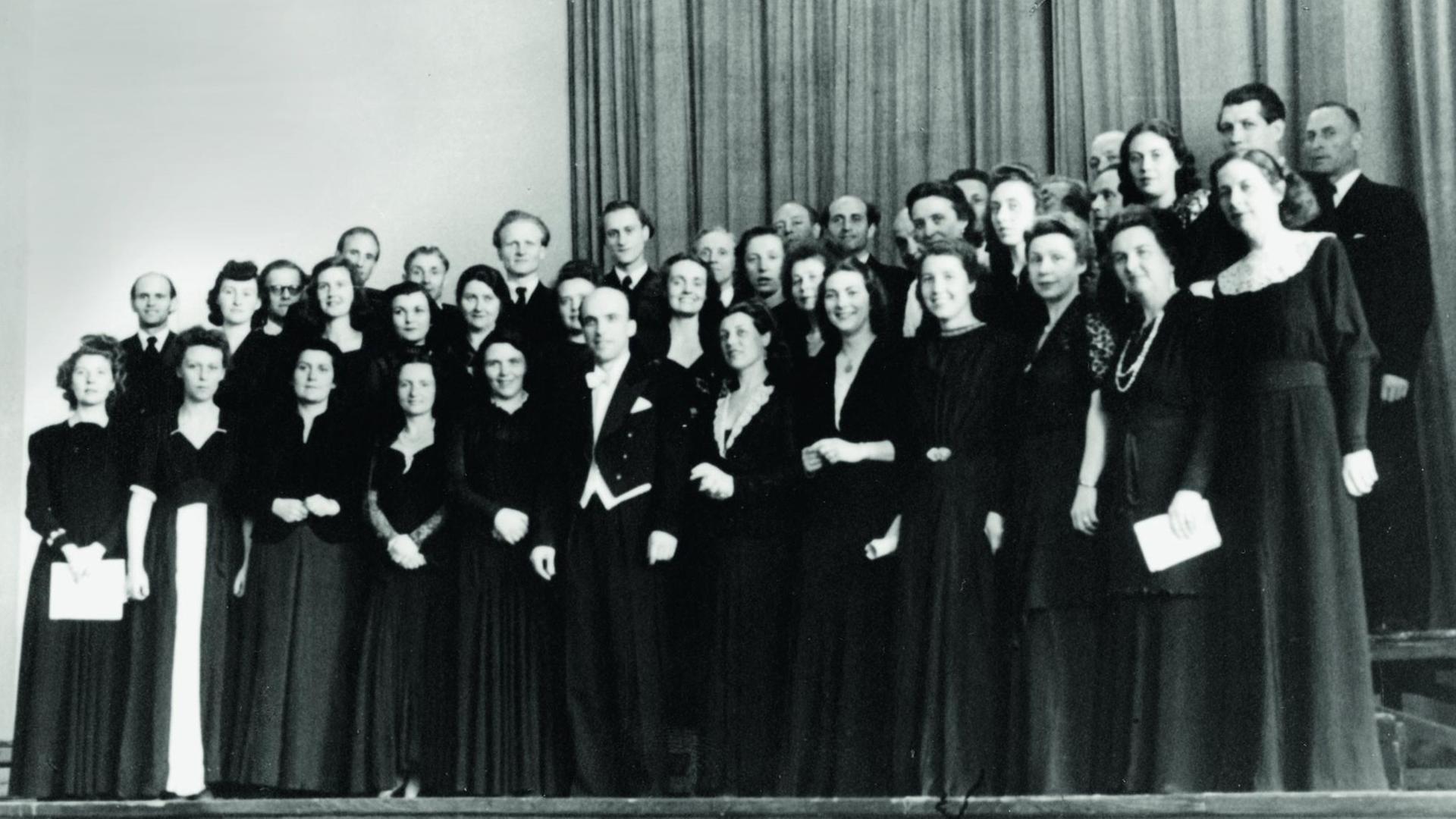 Der RIAS Kammerchor auf einem schwarz-weiß-Foto in schwarzer Konzertkleidung, in der Mitte der Dirigent Herbert Froitzheim (im Frack) Aufnahme von 1949