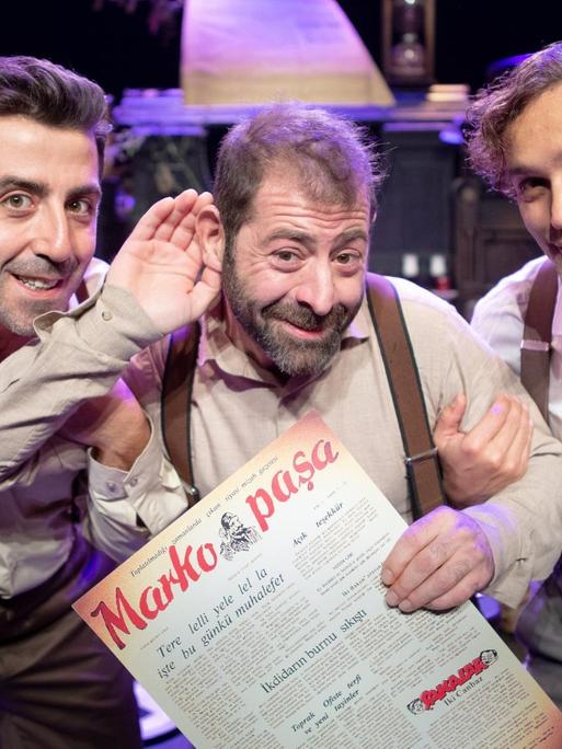 Fatih Koyunoğlu, Erdem Akakçe, Bülent Çolak vom Theater Tiyatroadam gucken in die Kamera und halten jeweils eine Hand hinter die Ohren, als ob sie etwas Bestimmtes hören wollen.