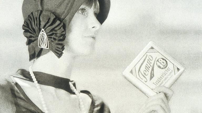 Eine Frau in 1920er-Jahre-Mode mit einem Päckchen Tempotaschentücher.