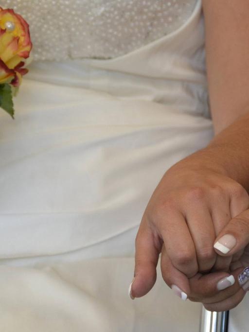 Zwei weibliche Hände berühren sich, sitzend, weißes Hochzeitskleid