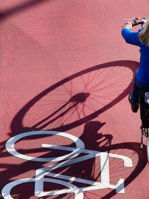 Ein Fahrrad ist auf einem neuen, roten Radweg auf der Schlossstrasse in Steglitz aufgemalt. Eine Frau faehrt mit ihrem Rad auf dem Radweg.