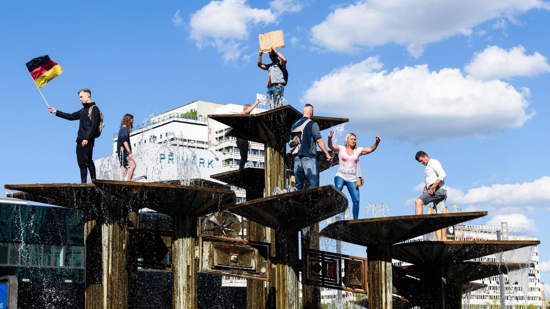 Demonstration gegen die Corona-Verordnungen am Berliner Alexanderplatz. Menschen stehen in einem Springbrunnen. Ein Mann hält die deutsche Flagge in der Hand.
