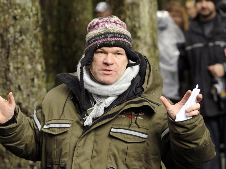 Regisseur Uwe Boll hat eine Strickmütze auf und zeigt die Handflächen.