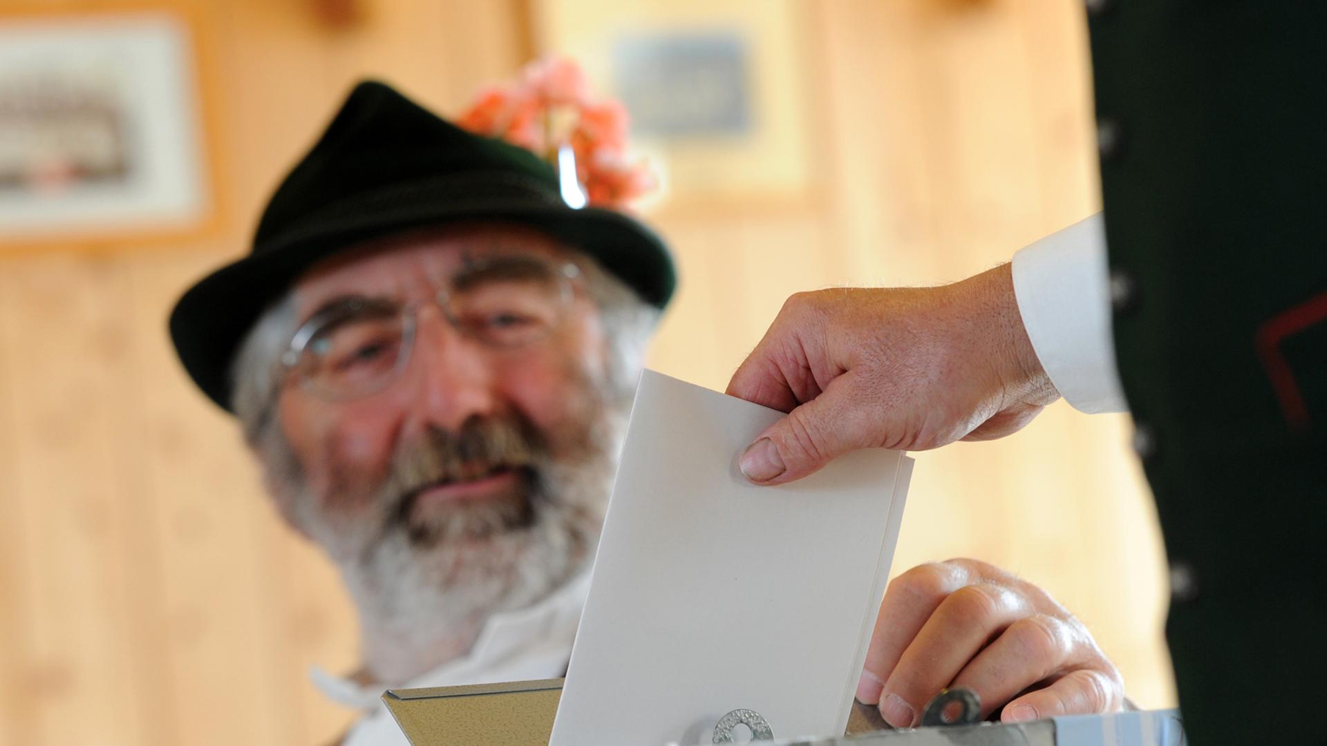 Ein Wahlhelfer in bayerischer Tracht mit Hut verfolgt am 25.05.2014 in Deining (Bayern) in einem Wahllokal den Einwurf eines Wahlzettels in die Wahlurne.