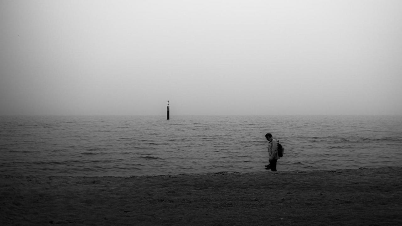 Ein Mann im Schattenriss steht am Meer,