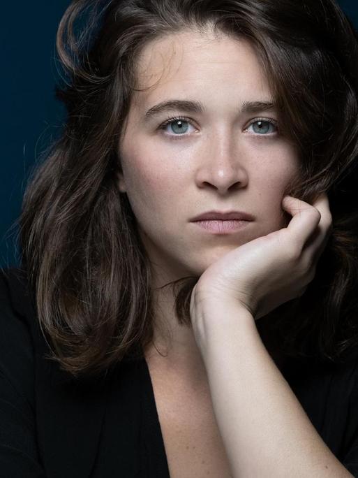 Emma Becker schaut, ihren Kopf auf die Hand gestützt, in die Kamera