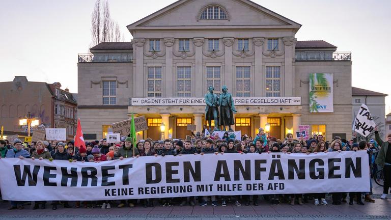 "Wehret den Anfängen - Keine Regierung mit Hilfe der AFD" steht auf einem Transparent, das Demonstranten vor dem Theater und dem Goethe- und Schillerdenkmal halten. Die Menschen demonstrieren gegen den neuen Ministerpräsidenten von Thüringen.