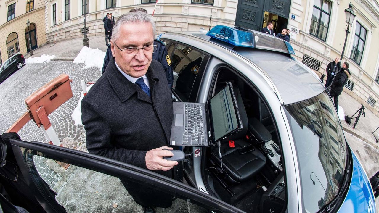 Der Bayerische Innenminister Joachim Herrmann mit einem Fahrzeug der Bayerischen Grenzpolizei in einer Ausstellung zu ihrer Ausrüstung und ihrer Fähigkeiten. Er hält einen Laptop in der Hand.