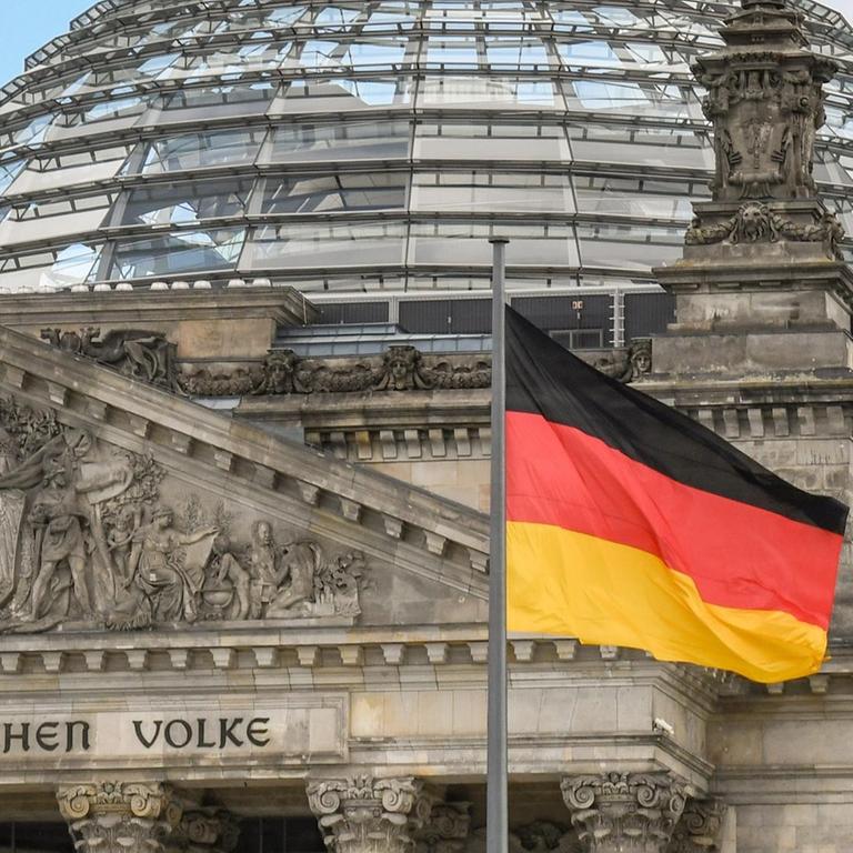 Die Bundesflagge weht vor dem Portal des Reichstagsgebäude in Berlin mit dem Schriftzug: Dem Deutschen Volke.