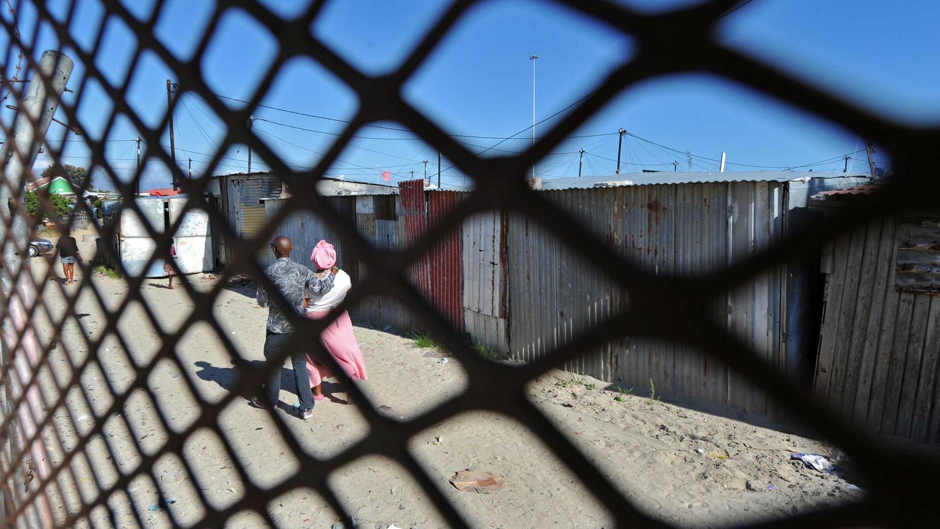 Ein Paar spaziert vor ärmlichen Hütten im Township Khayelitsha nahe Kapstadt.