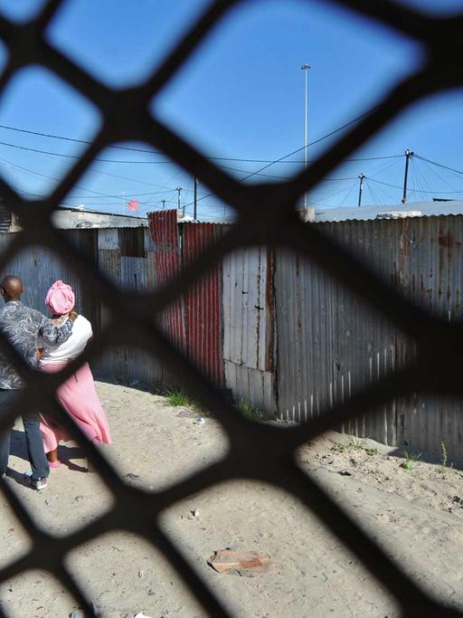 Ein Paar spaziert vor ärmlichen Hütten im Township Khayelitsha nahe Kapstadt.