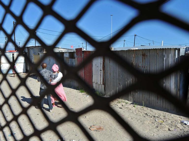 Ein Paar spaziert vor ärmlichen Hütten im Township Khayelitsha nahe Kapstadt.