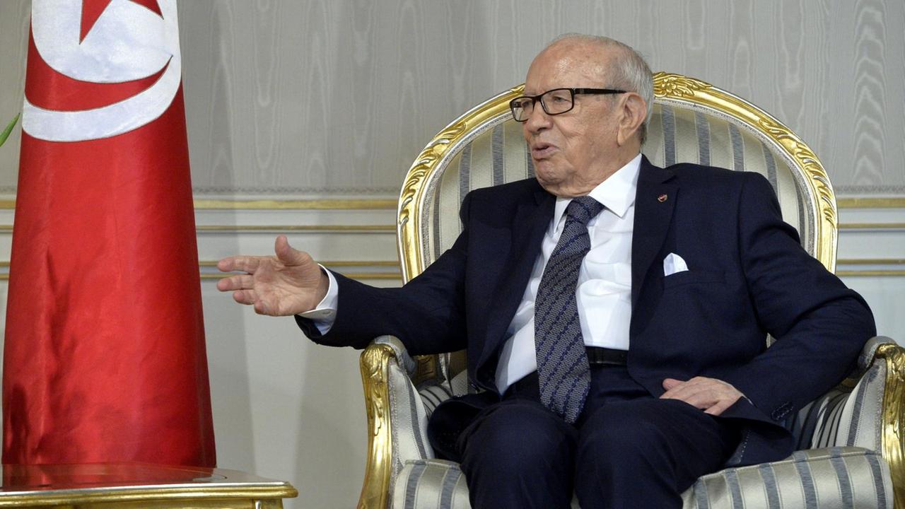 Tunesiens Präsident Béji Caïd Essebsi während eines Staatsempfangs in der Hauptstadt Tunis. Sitzend im Sessel neben einer Staatsflagge.