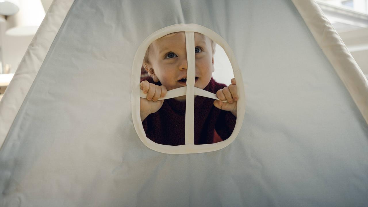 Ein Kind sitzt in einem Spielzelt in einem Zimmer.
