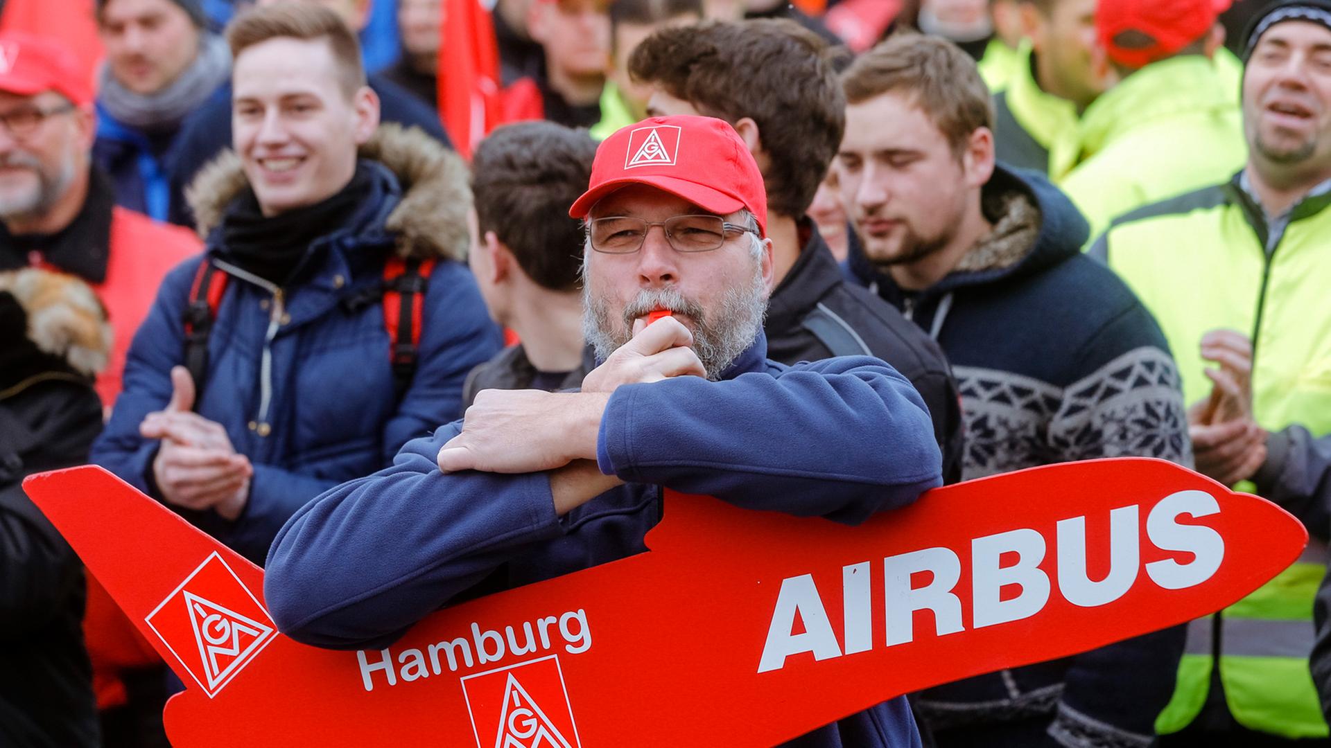 Auf einer Demonstration hält ein Mann ein rotes Schild in Flugzeugform mit der Aufschrift Airbus.