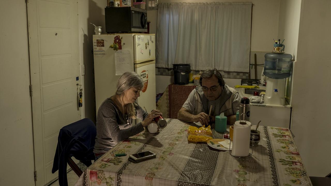 Ein älteres Paar sitzt in der Küche an einem Tisch. Im Hintergrund steht ein großer Kühlschrank.