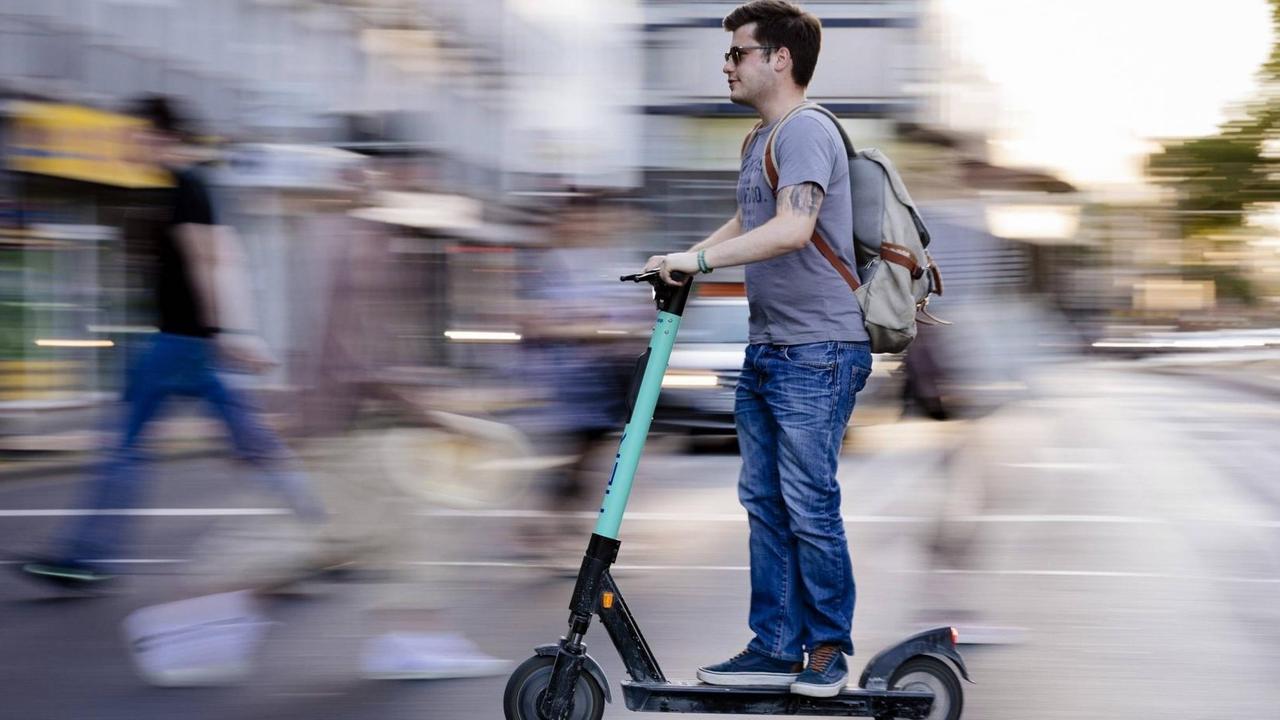 Ein Mann auf einem E-Scooter fährt über die Straße. Ein Mann auf einem E-Scooter fährt über die Straße.