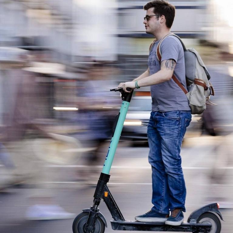 Ein Mann auf einem E-Scooter fährt über die Straße.