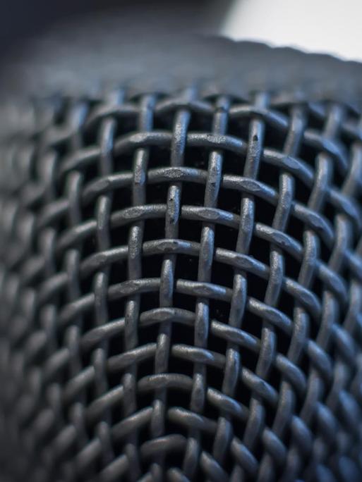 Das Bild zeigt eine Detail-Nahaufnahme eines Mikrofons - nur ein kleiner Teil der Mikrofonoberfläche ist fokussiert und scharf, der Rest des Mikrofons verschwindet in Unschärfe.
