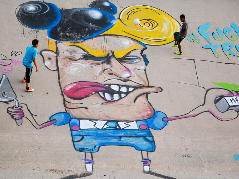 Kinder spielen am 23.06.2016 neben einer Graffiti-Karikatur, die Donald Trump im Flussbett des Rio Grande, zeigt.
