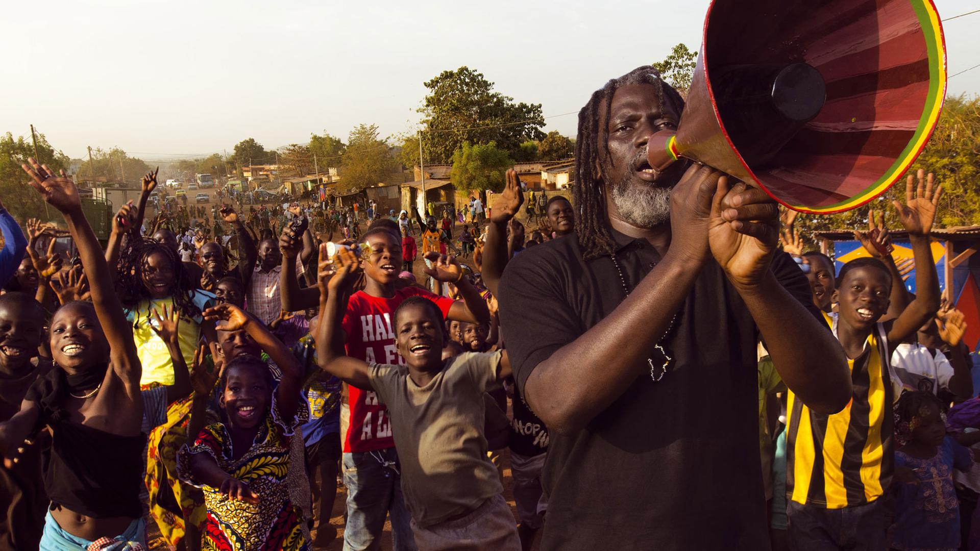 Mit einem Megafon steht der Ivorer Tiken Jah Fakoly vor einer Gruppe von Jugendlichen.
