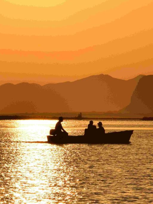 Sizialianische Küste: Silhouette eines Boots vor orangenem Sonnenuntergang. 