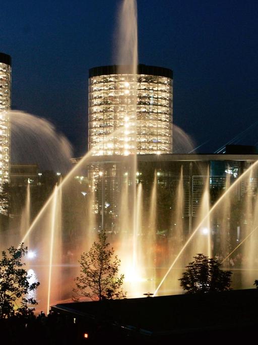 Licht- und Wasserspiele vor dunkelblauem Nachthimmel und zwei beleuchteten Hochhäusern in der Autostadt Wolfsburg