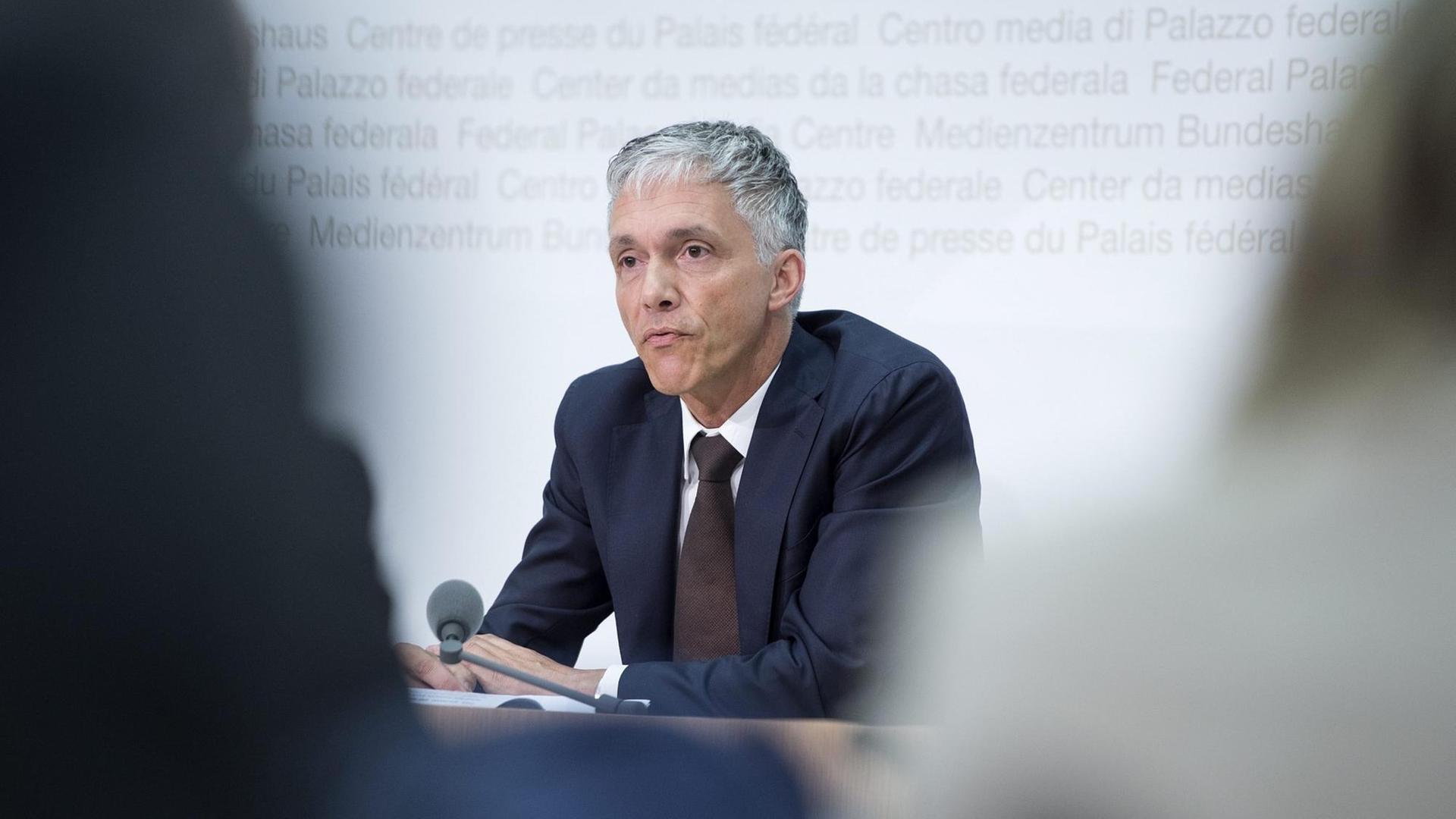 Foto vom oberste Strafermittler der Schweiz, Michael Lauber, bei einer Pressekonferenz durch zwei Journalisten hindurch