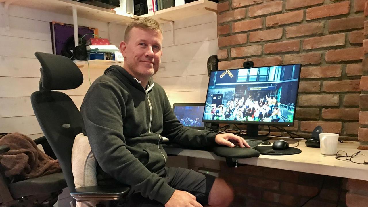 Ein Mann in kurzen Hosen und Sweater sitzt vor seinem PC am Schreibtisch.