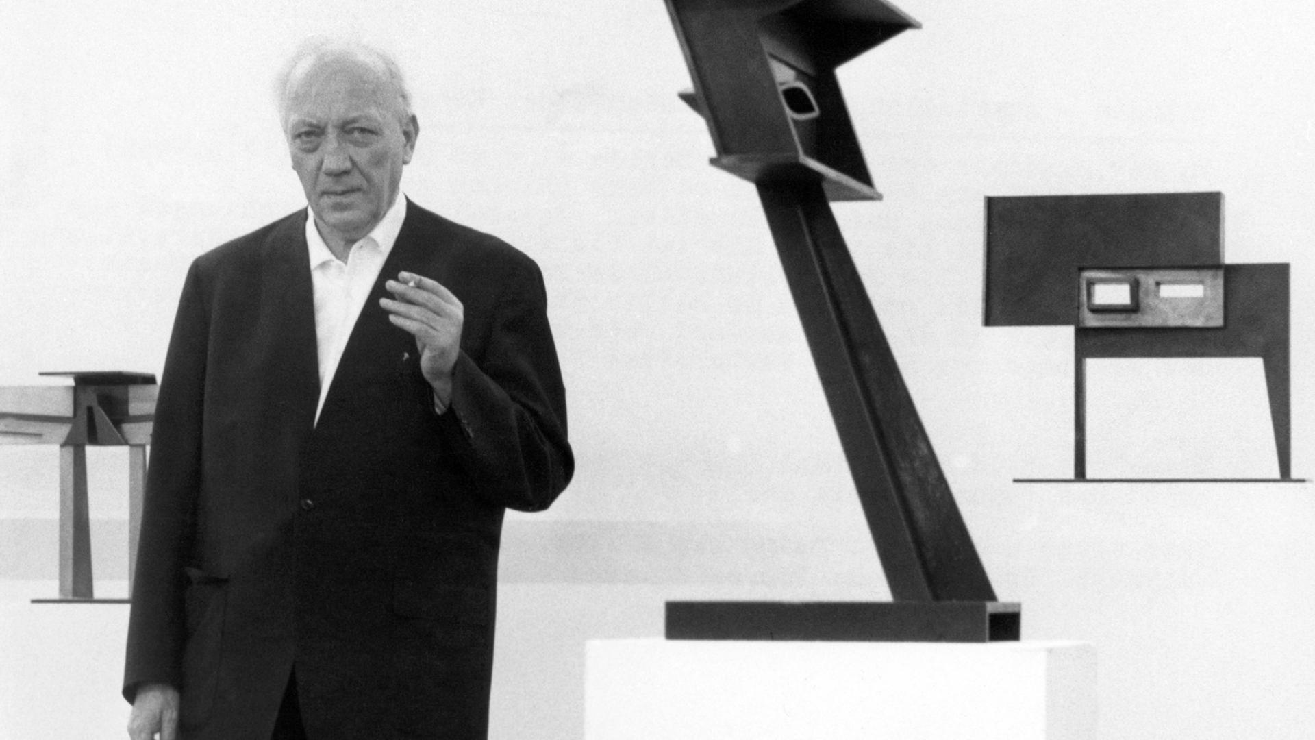 Der Bildhauer Hans Uhlmann neben seinen Plastiken "Fetisch 1963" und "Stahlplastik 1961" am 15.03.1968 in der Akademie der Künste in Berlin.