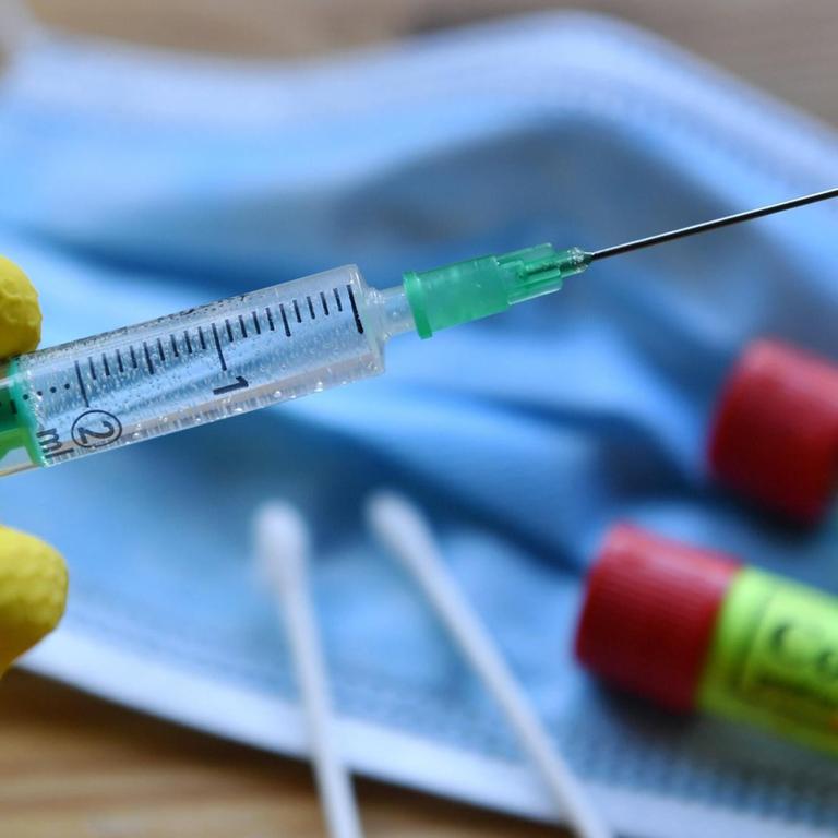 Eine Hand in Gummihandschuhe gehüllt hält eine Einwegspritze mit Impfstoff zur Injektion mit einer Kanüle - Symbolbild Corona-Impfstoff