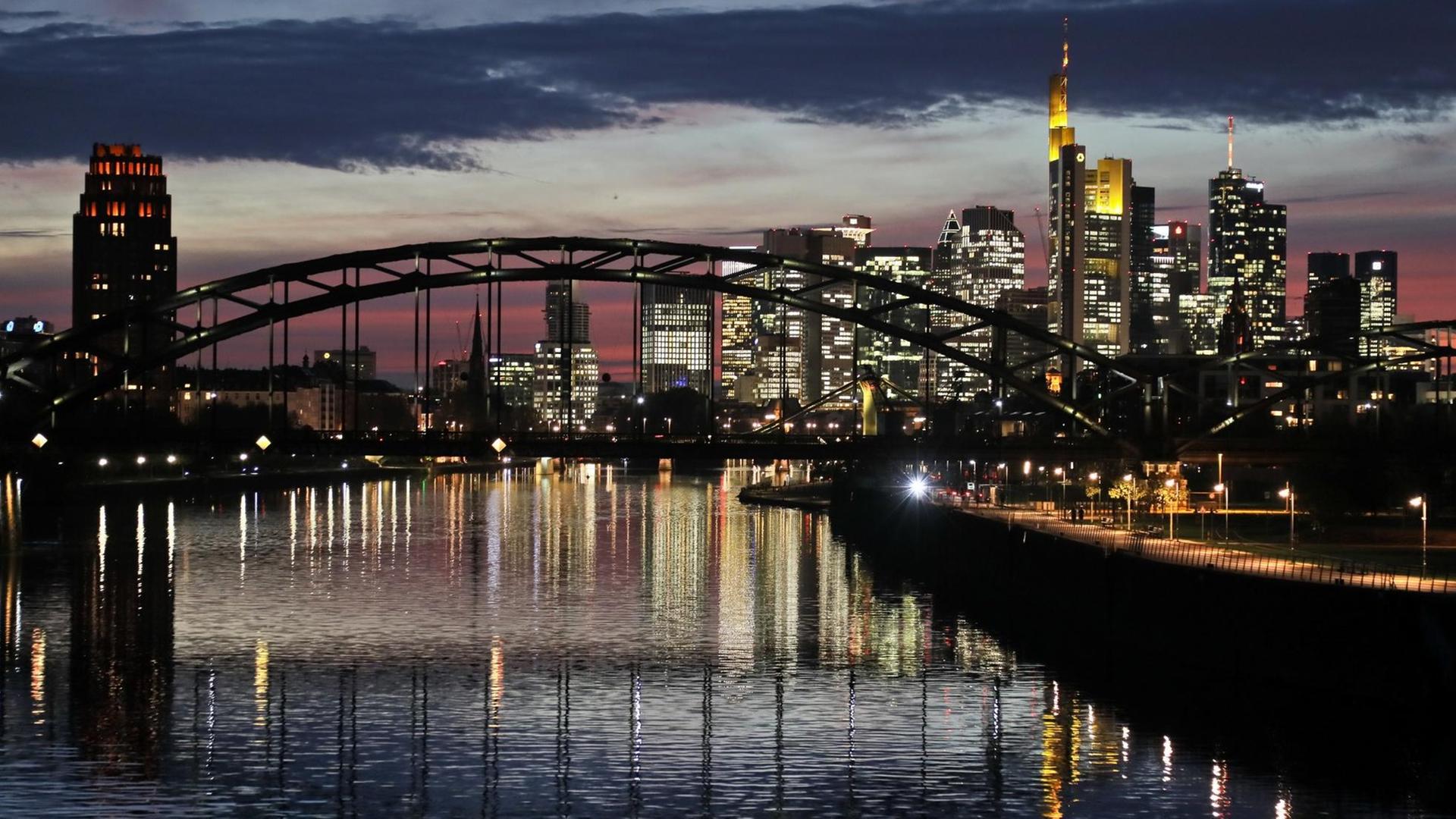 Die Skyline von Frankfurt am Main mit vielen Bankengebäuden spiegelt sich am Abend im Main