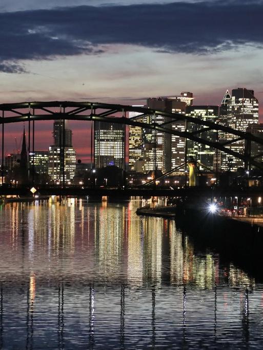 Die Skyline von Frankfurt am Main mit vielen Bankengebäuden spiegelt sich am Abend im Main