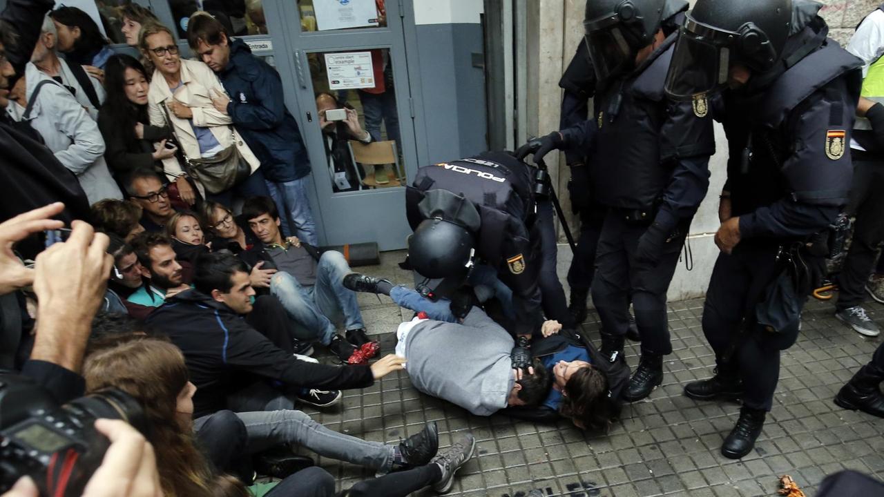 Spanische Polizisten setzen vor einem Wahllokal in Barcelona zwei Menschen fest.